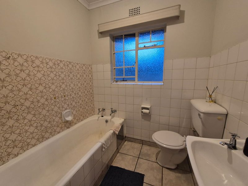 A dated bathroom featuring a standard bathtub, pedestal basin, and toilet with original wall tiling and tiled flooring.