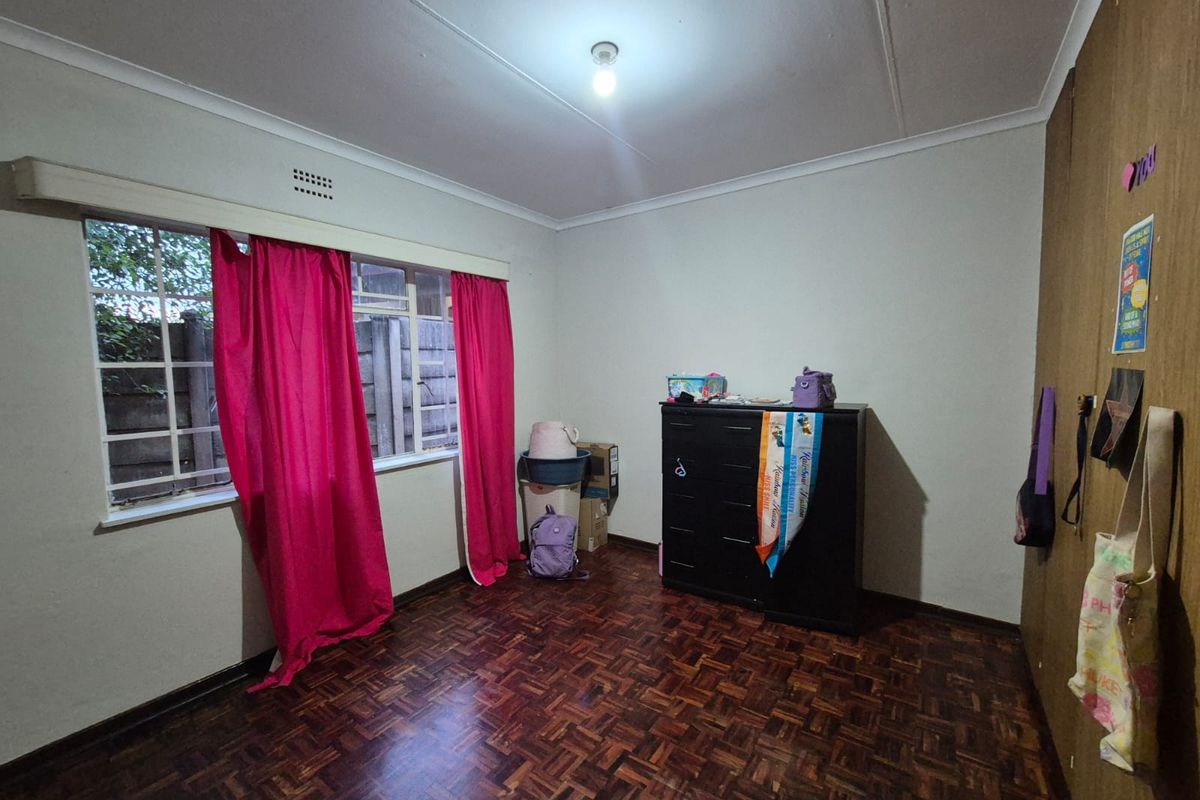 A bedroom featuring classic parquet flooring, built-in cupboards, and a window with security bars, offering a functional space with potential for modernization.