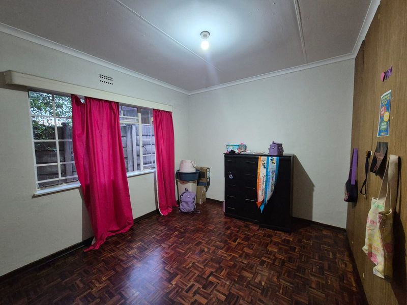 A bedroom featuring classic parquet flooring, built-in cupboards, and a window with security bars, offering a functional space with potential for modernization.