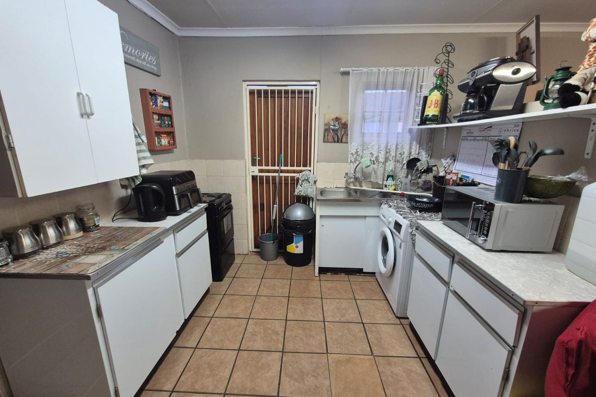 A functional kitchen featuring built-in cabinetry, tiled flooring, and a dedicated laundry area with plumbing connections for a washing machine.