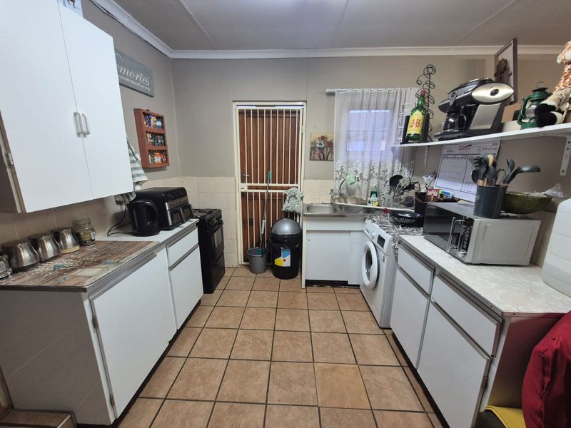 A functional kitchen featuring built-in cabinetry, tiled flooring, and a dedicated laundry area with plumbing connections for a washing machine.