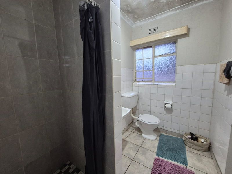 A functional bathroom featuring a shower enclosure, toilet, and wash basin, with visible signs of ceiling water damage and dated tile finishes.