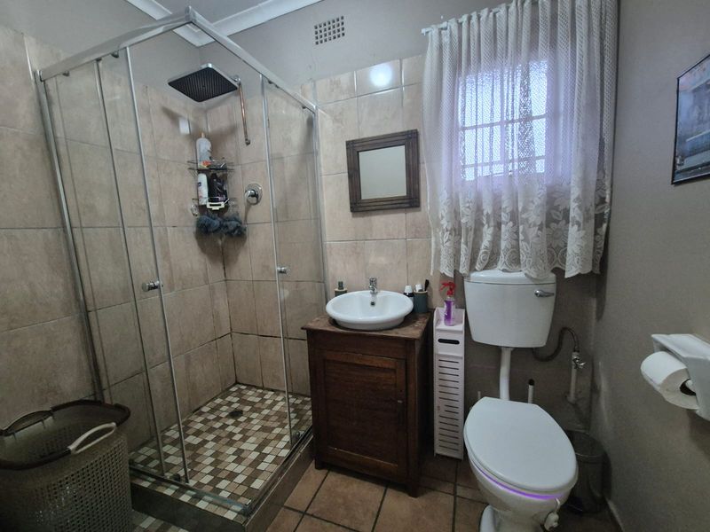 A functional bathroom featuring a glass-enclosed shower with a rain shower head, a vanity with a ceramic basin, and a standard toilet.