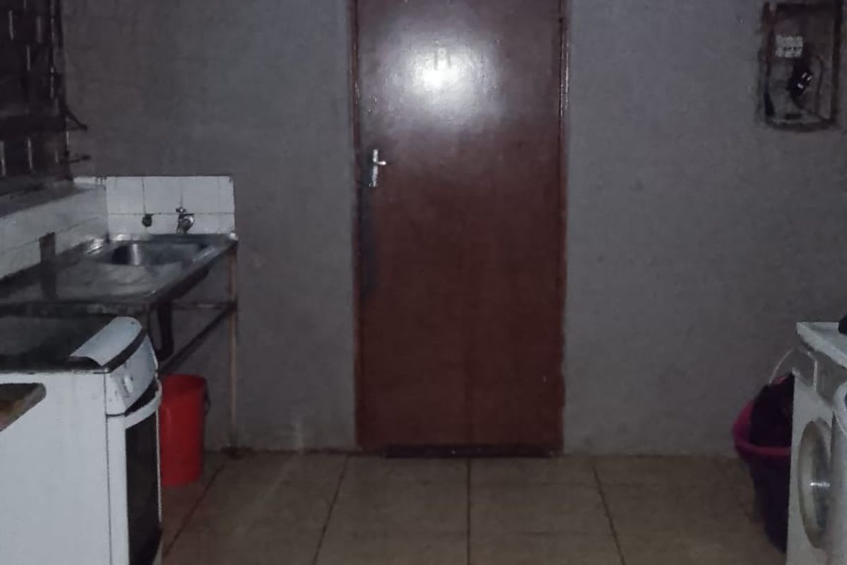A basic kitchen area featuring tiled flooring, a stainless steel sink, and unfinished wall surfaces, requiring cosmetic updates and improved lighting.