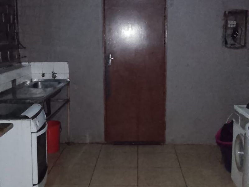 A basic kitchen area featuring tiled flooring, a stainless steel sink, and unfinished wall surfaces, requiring cosmetic updates and improved lighting.