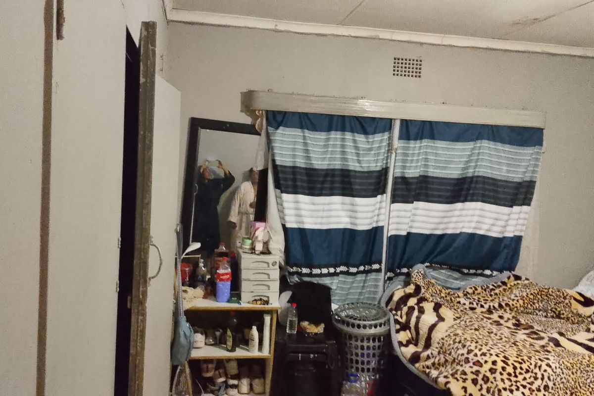 A bedroom featuring a ventilation grille and basic ceiling cornice, currently showing signs of wear and requiring cosmetic updates to the walls and finishes.