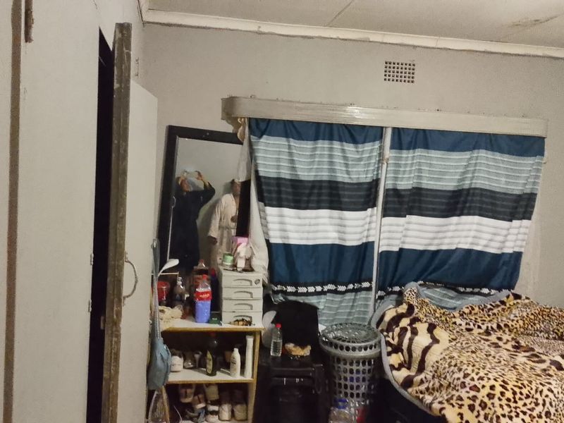 A bedroom featuring a ventilation grille and basic ceiling cornice, currently showing signs of wear and requiring cosmetic updates to the walls and finishes.