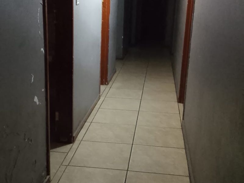 A narrow interior hallway featuring tiled flooring and multiple internal doorways, currently showing significant signs of wear to the walls and ceiling.