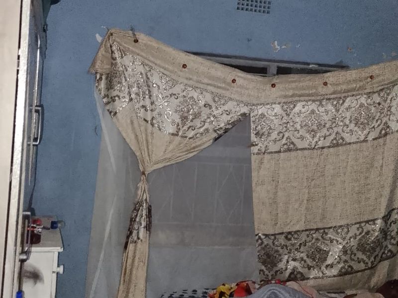 A bedroom featuring tiled flooring and a ventilation brick, currently showing signs of significant wear including peeling paint and damaged wall surfaces.