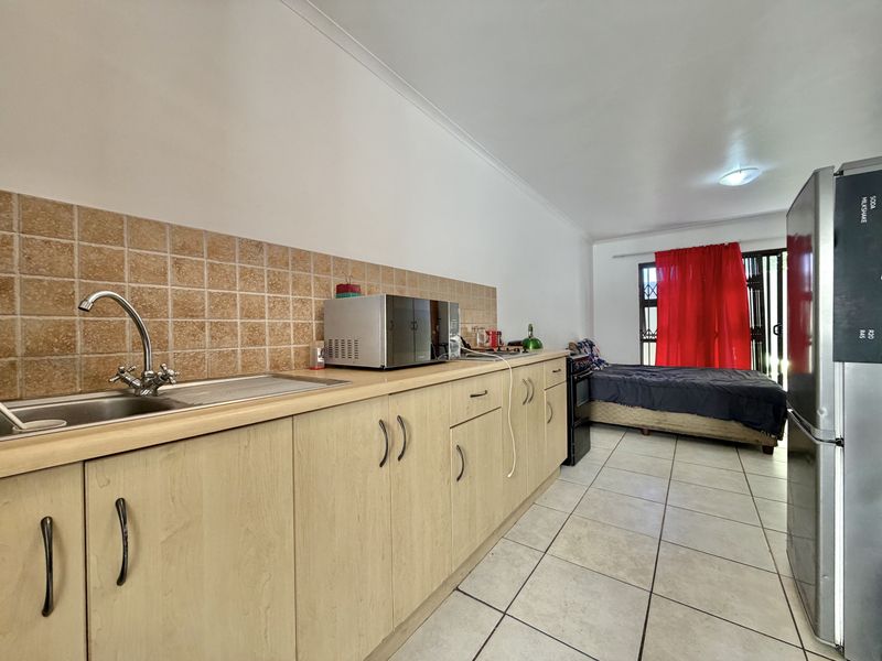 Open-plan studio apartment featuring a functional kitchen area with laminate cabinetry, tiled backsplash, and direct access to a patio area.