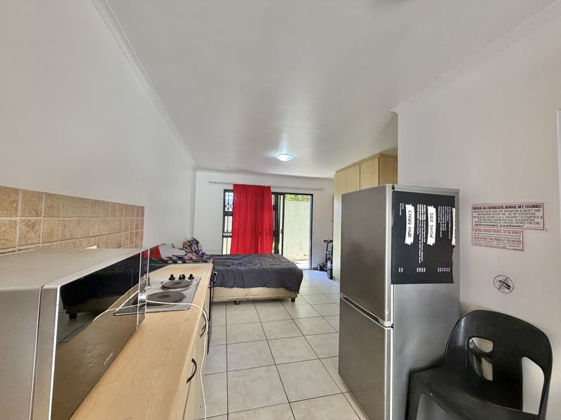 Open-plan studio apartment featuring a compact kitchen area with built-in cabinetry and hob, leading to a living and sleeping space with sliding door access.