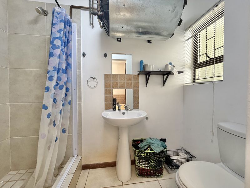 Compact bathroom featuring a pedestal basin, toilet, and shower enclosure with tiled finishes and an exposed electric water heater.