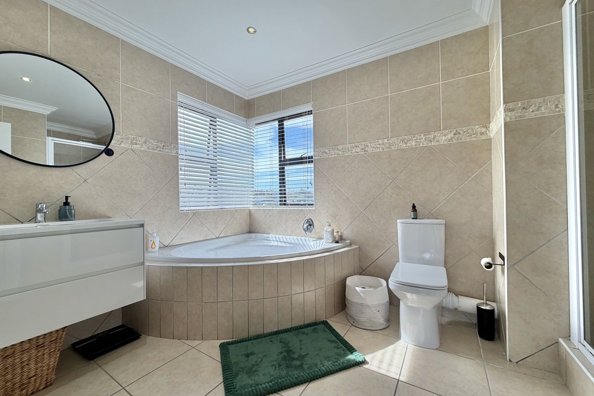 A well-lit bathroom featuring a corner bathtub, wall-mounted vanity, and neutral ceramic tiling throughout, offering a functional and clean space.