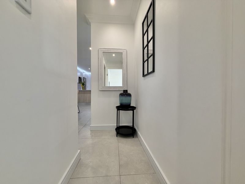 A bright and clean hallway featuring neutral tiled flooring, crisp white walls, and recessed downlighting, leading into an open-plan living area.