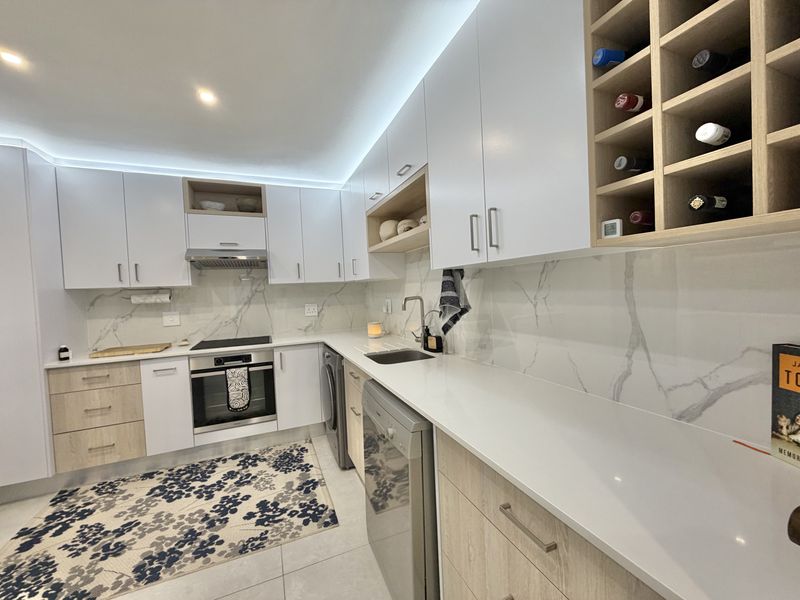 Modern kitchen featuring sleek white cabinetry, light wood accents, marble-look splashbacks, integrated wine storage, and high-quality built-in appliances.
