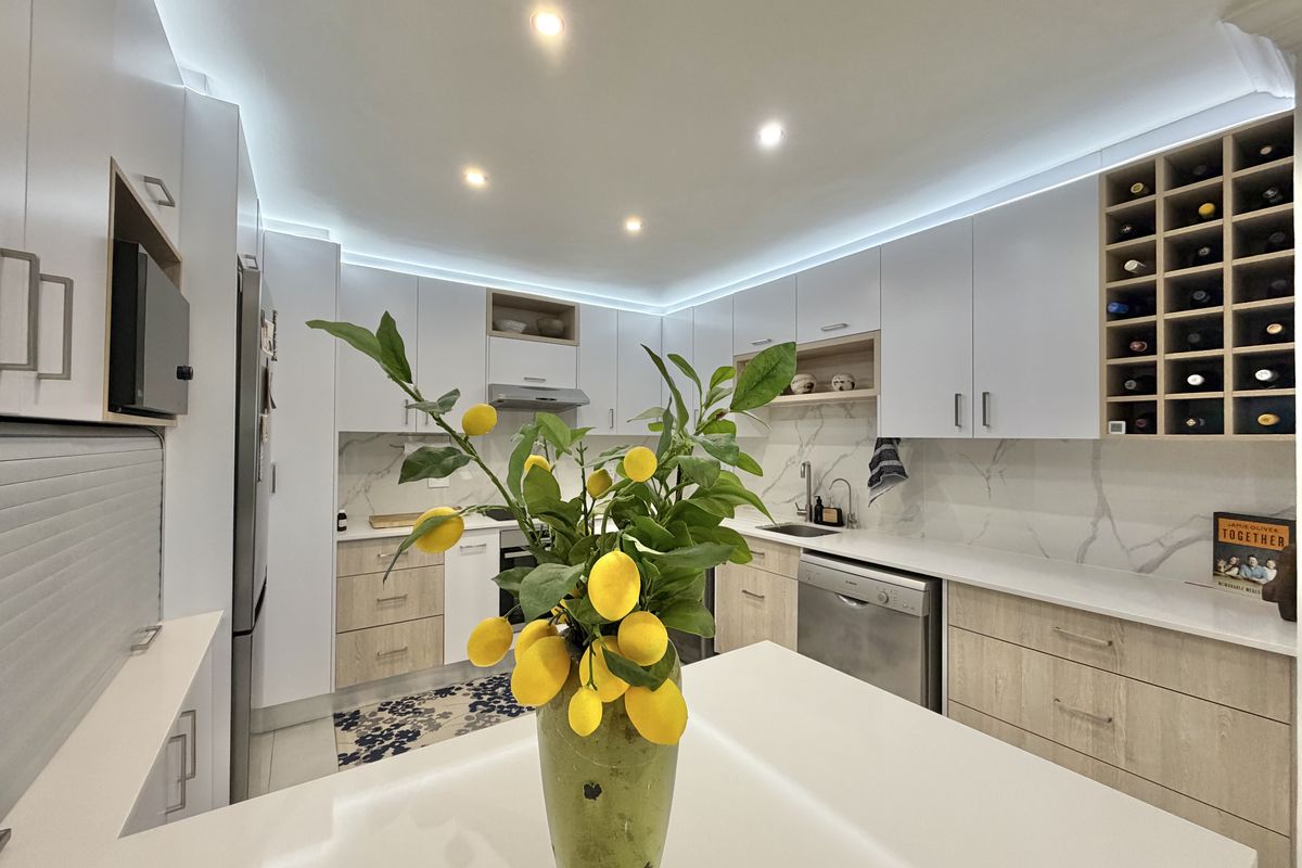 Modern kitchen featuring sleek white and wood-tone cabinetry, stone countertops, marble-look splashback, integrated wine storage, and contemporary recessed LED lighting.