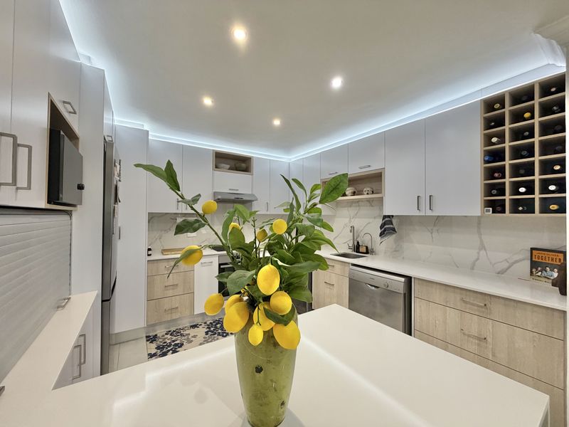 Modern kitchen featuring sleek white and wood-tone cabinetry, stone countertops, marble-look splashback, integrated wine storage, and contemporary recessed LED lighting.