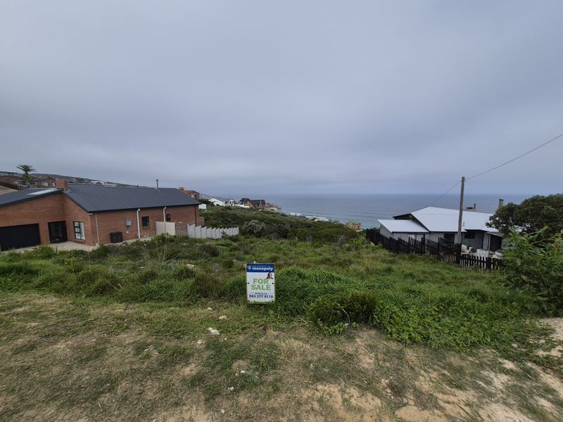 A vacant residential plot featuring a scenic coastal view, situated in a developed neighborhood with surrounding residential properties.