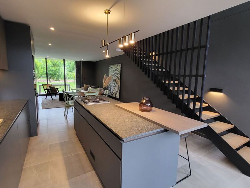 Modern open-plan kitchen and living area featuring a central island with gas cooktop, sleek cabinetry, and a striking staircase with integrated lighting.