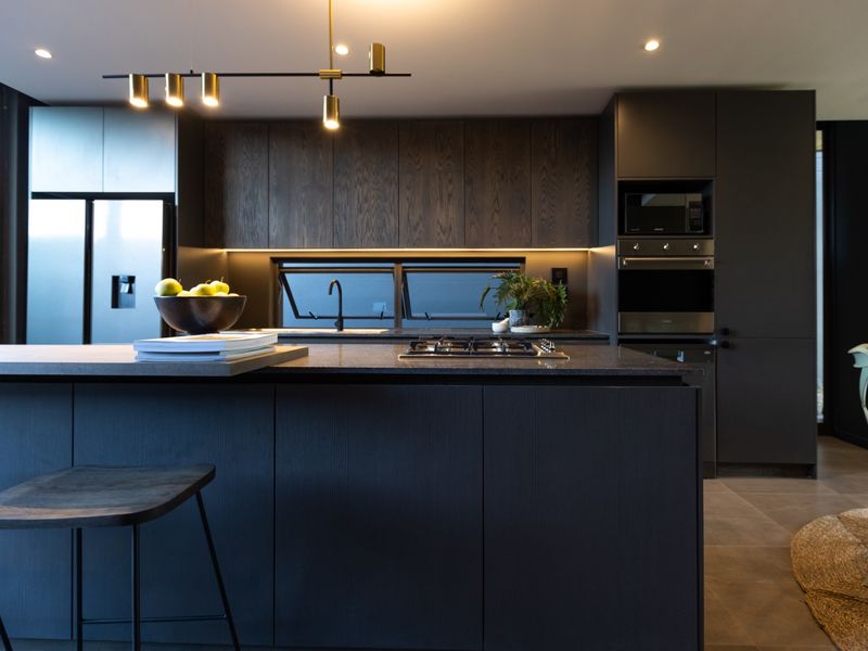 Modern kitchen featuring dark wood cabinetry, stone island countertop, integrated appliances, and sleek contemporary lighting in a high-end finish.