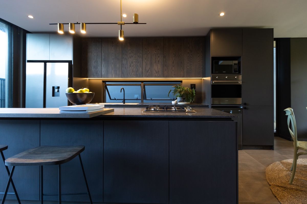 Modern kitchen featuring dark wood cabinetry, stone island countertop, integrated appliances, and sleek contemporary lighting in a high-end finish.