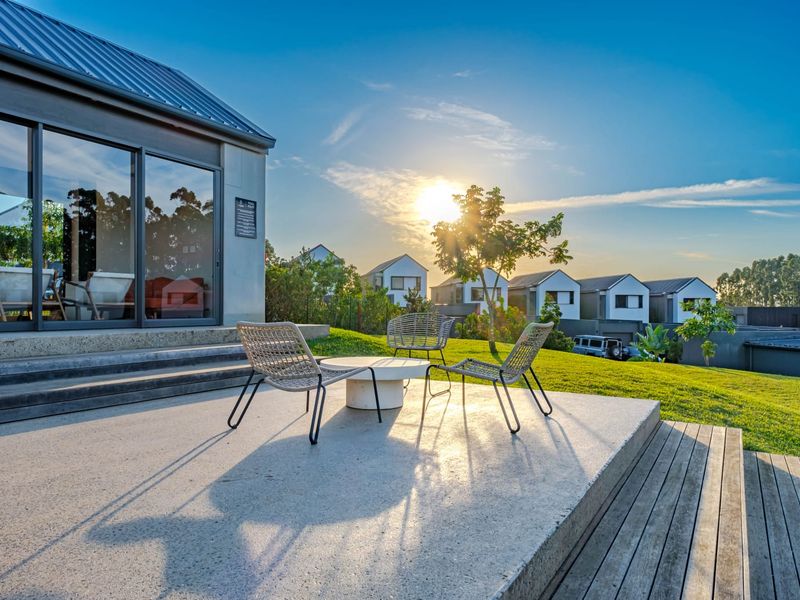A modern concrete patio area featuring sliding glass doors and timber steps, overlooking a landscaped garden and surrounding townhouse development.