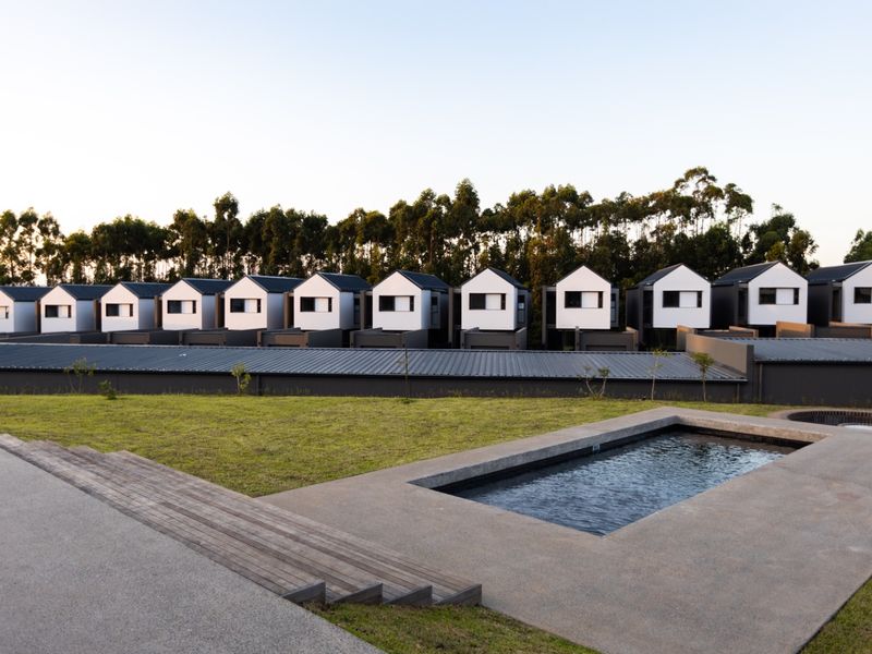 A modern outdoor pool area featuring a rectangular swimming pool, timber decking, and concrete paving, set against a backdrop of contemporary townhouse units.