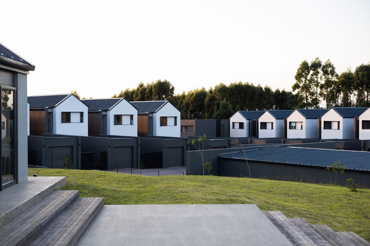 A view of the rear exterior of the townhouse complex, featuring modern architectural design, timber decking, concrete patio, and well-maintained lawn areas.