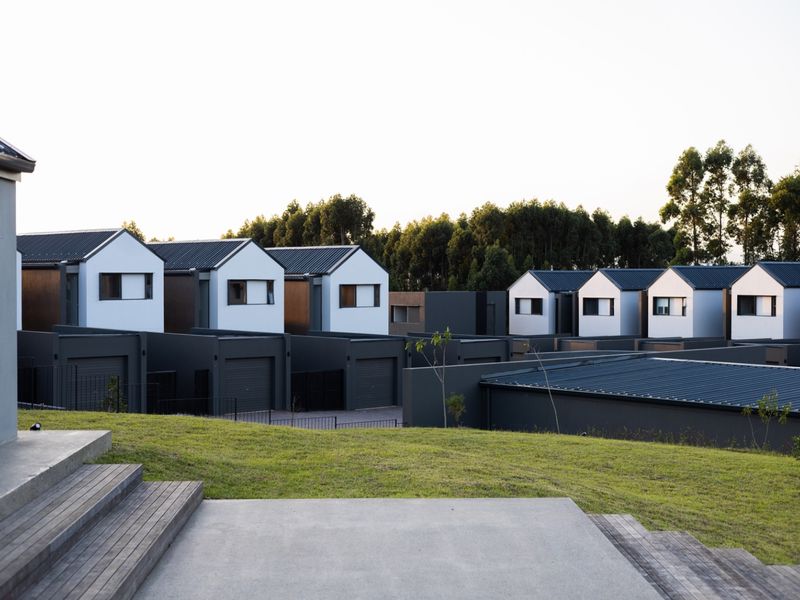 A view of the rear exterior of the townhouse complex, featuring modern architectural design, timber decking, concrete patio, and well-maintained lawn areas.