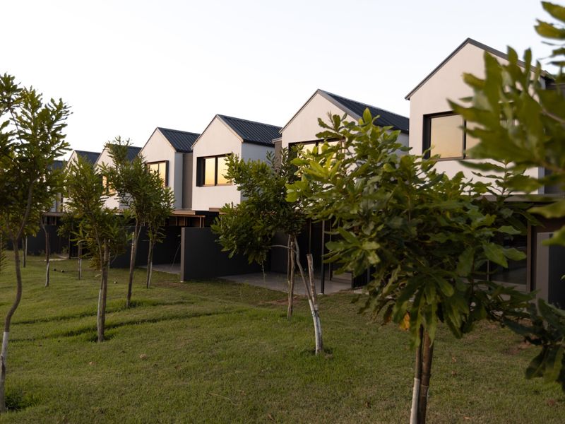 A row of modern townhouses featuring pitched metal roofs, clean architectural lines, and private ground-level patios overlooking a well-maintained communal garden area.