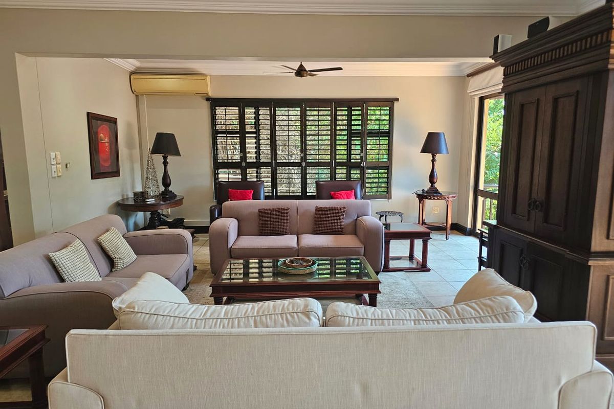Spacious living room featuring tiled flooring, crown molding, a ceiling fan, and plantation shutters, providing a comfortable and well-maintained living space.