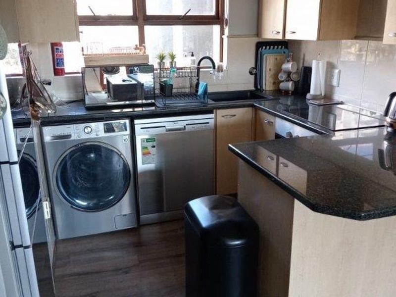 Compact kitchen featuring laminate cabinetry, granite countertops, tiled backsplash, and integrated space for laundry and dishwashing appliances.