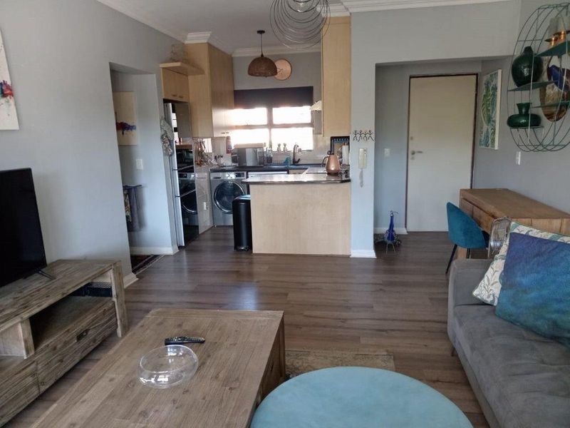 An open-plan living and kitchen area featuring laminate flooring, neutral wall tones, and a functional kitchen peninsula with built-in cabinetry.
