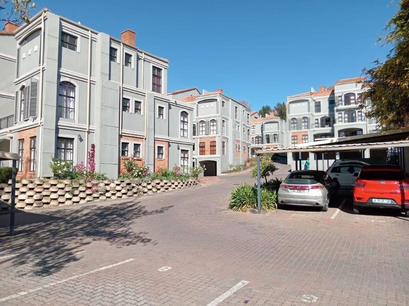 Exterior view of a multi-story townhouse complex featuring paved driveway access and covered carport parking areas.