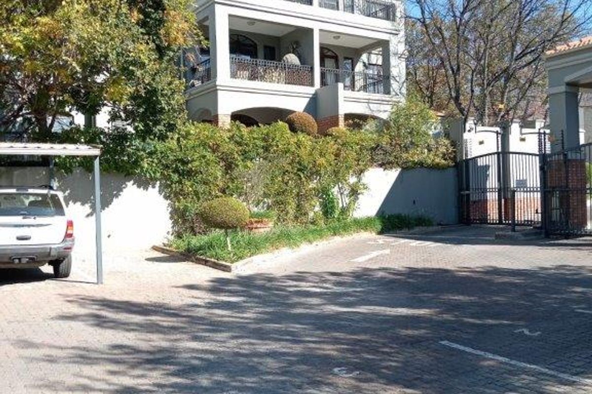 Front view of a multi-story townhouse complex featuring paved parking, secure gated access, and private balconies.