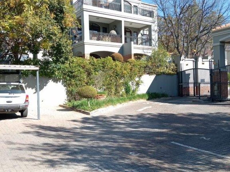 Front view of a multi-story townhouse complex featuring paved parking, secure gated access, and private balconies.