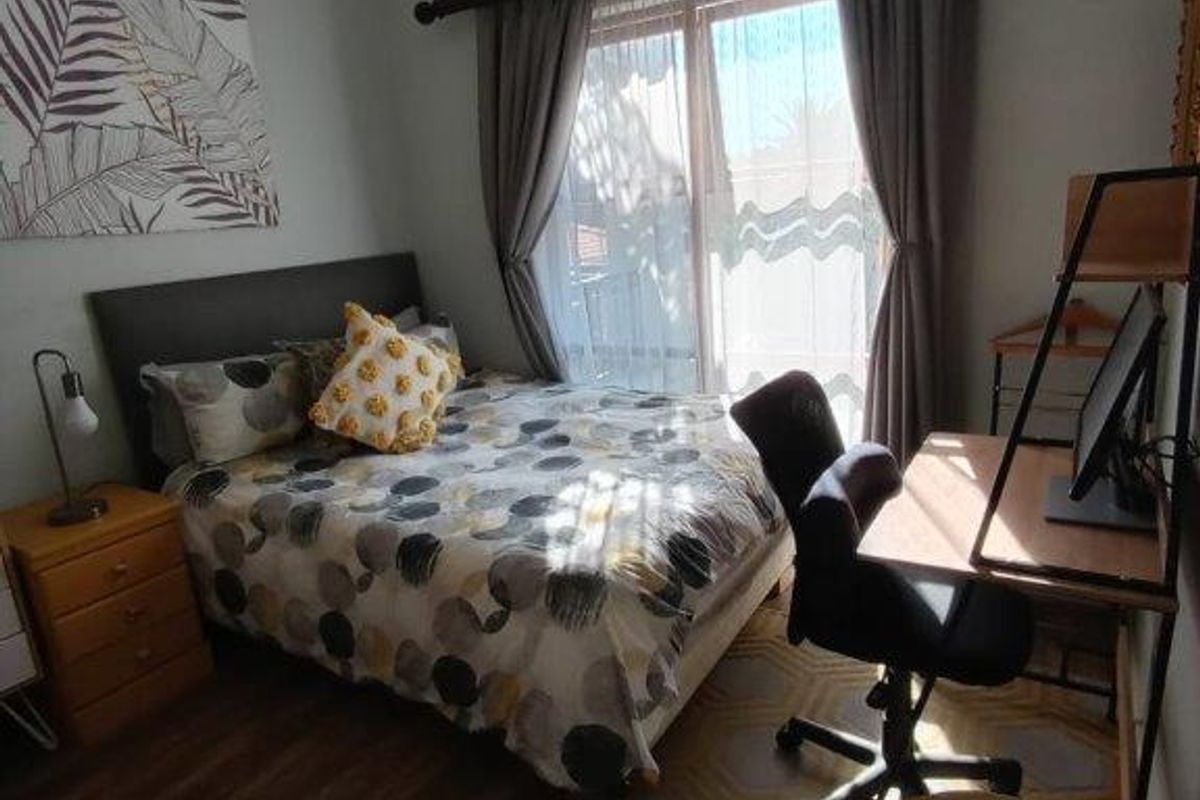 A cozy bedroom featuring laminate flooring, a ceiling fan, and a sliding glass door that provides natural light.