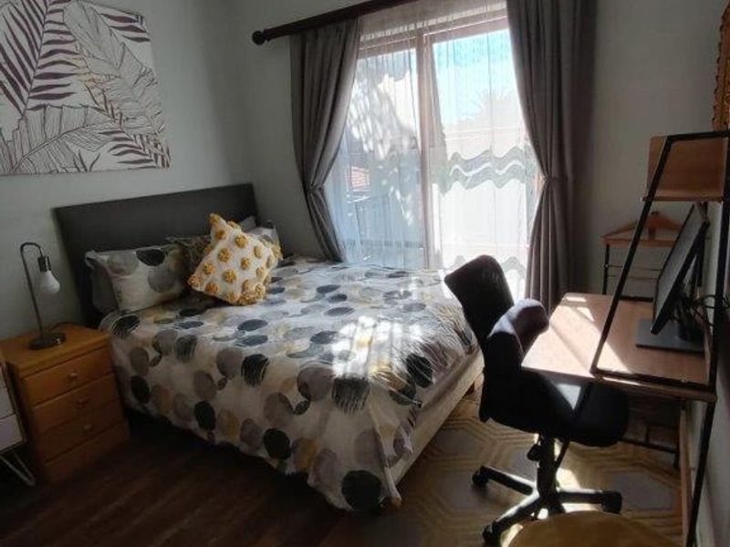 A cozy bedroom featuring laminate flooring, a ceiling fan, and a sliding glass door that provides natural light.