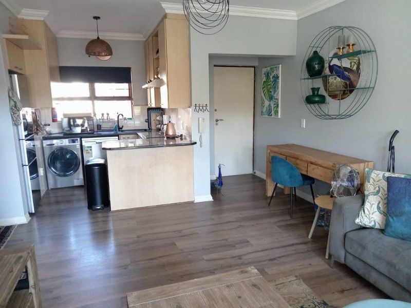 An open-plan living and kitchen area featuring modern laminate flooring, light wood cabinetry, and stone countertops in a well-maintained townhouse setting.