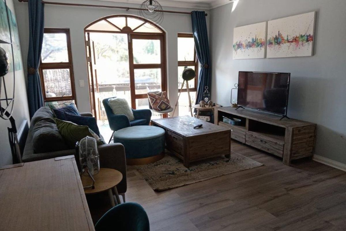 A comfortable living room featuring laminate flooring, crown molding, and an arched glass door providing access to an outdoor area.