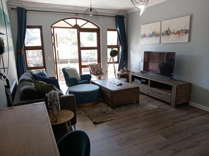 A comfortable living room featuring laminate flooring, crown molding, and an arched glass door providing access to an outdoor area.