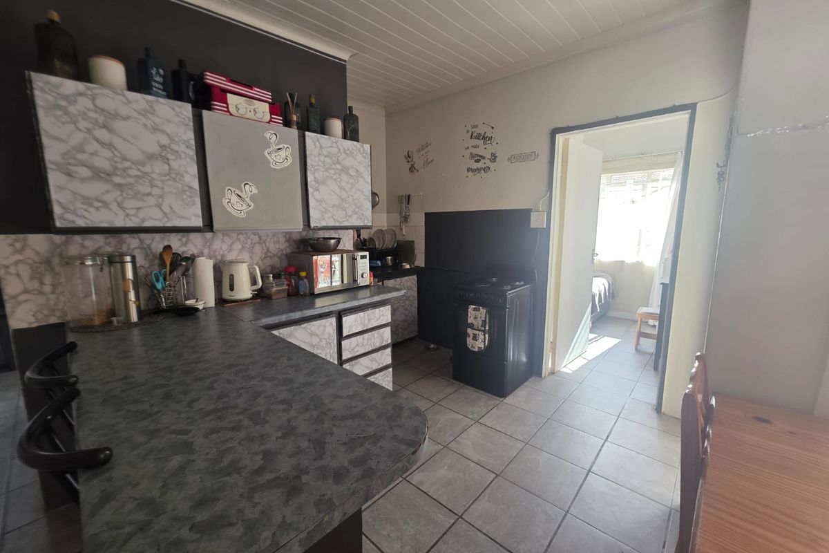A functional kitchen featuring laminate countertops, built-in cabinetry, and a freestanding stove, with tiled flooring and a timber panel ceiling.
