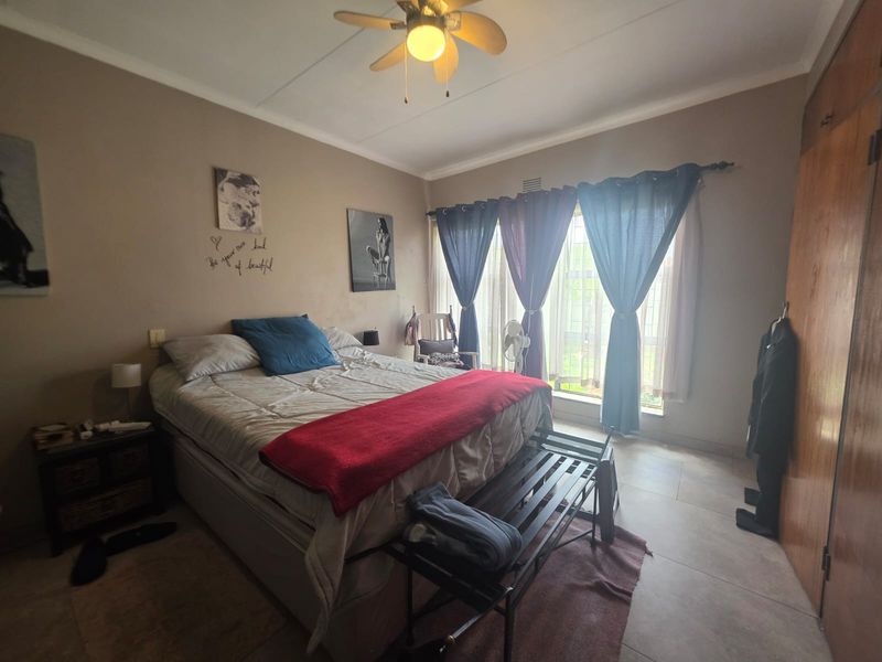 A bedroom featuring tiled flooring, a ceiling fan, and built-in wooden cupboards, offering a functional space with natural light.