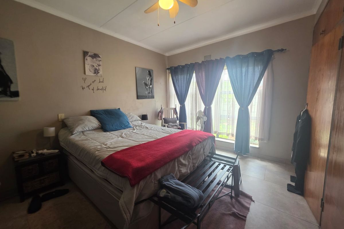 A bedroom featuring tiled flooring, a ceiling fan, and built-in wooden cupboards, offering a functional space with natural light.