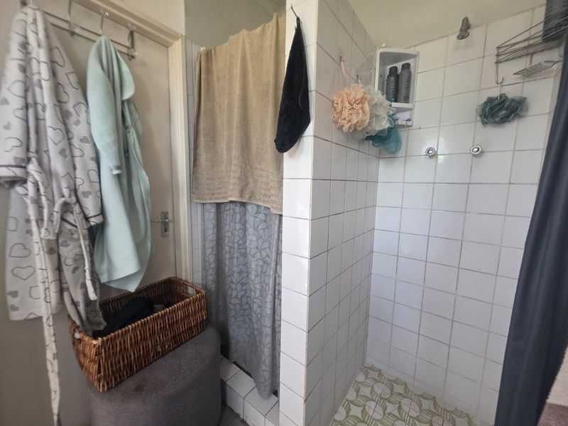 A functional bathroom shower area featuring white wall tiles, patterned floor tiles, and a built-in corner shelf.