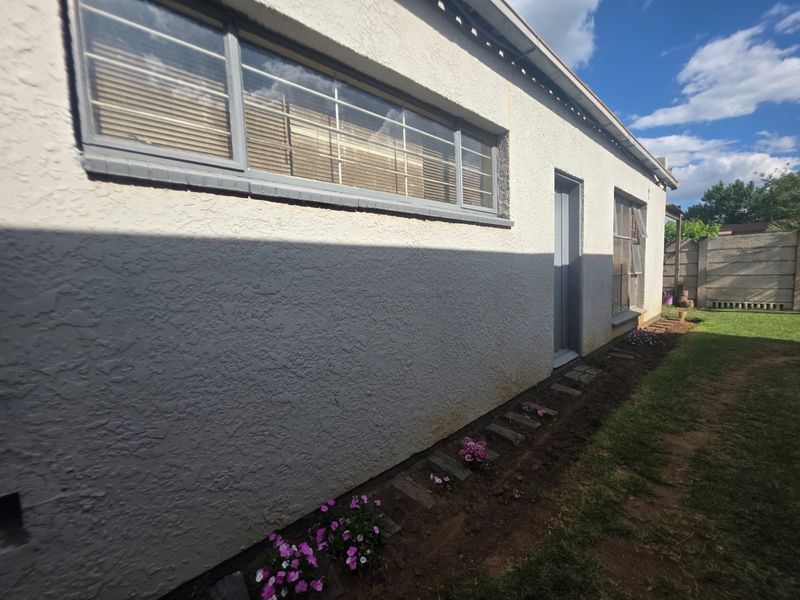 Rear exterior view of the property featuring a stucco facade, aluminium window frames with security bars, and a precast concrete boundary wall.