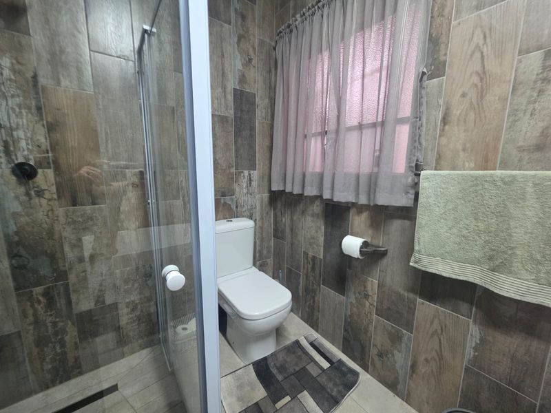 A modern bathroom featuring wood-look wall tiling, a glass-enclosed walk-in shower, and a standard toilet.