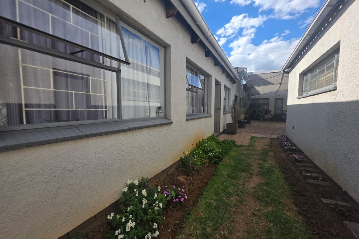 A view of the rear exterior of the property featuring plastered walls, steel-framed windows with security bars, and a paved pathway.