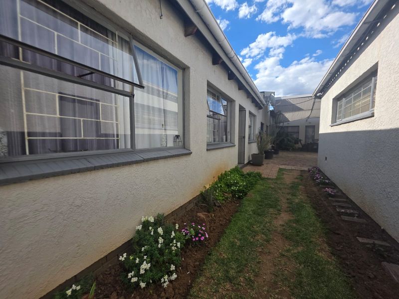 A view of the rear exterior of the property featuring plastered walls, steel-framed windows with security bars, and a paved pathway.