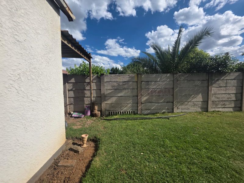 A rear garden area featuring a lawn and a precast concrete boundary wall with an attached covered patio structure.